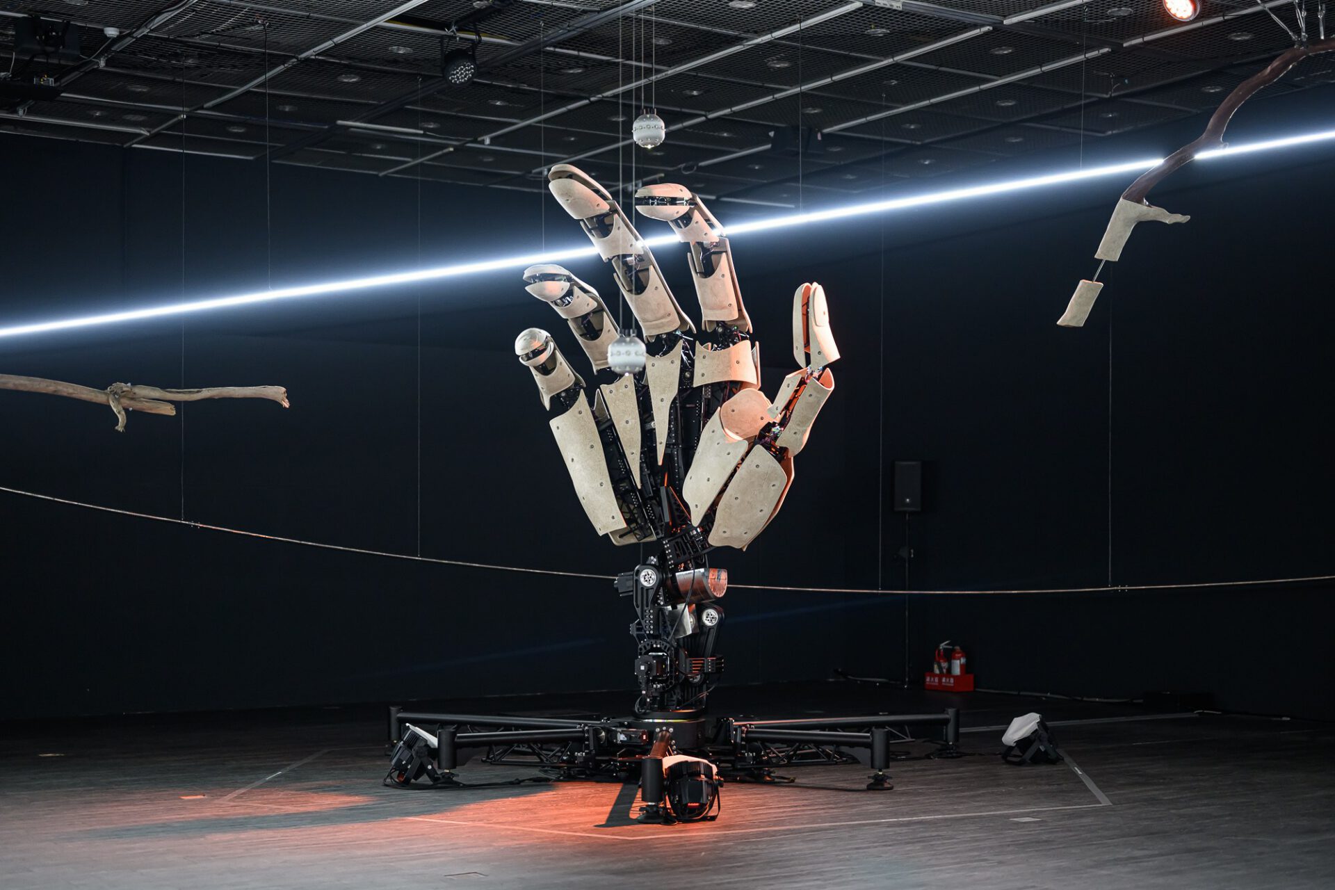 Upright mechanical hand beneath a curved white light in the installation.