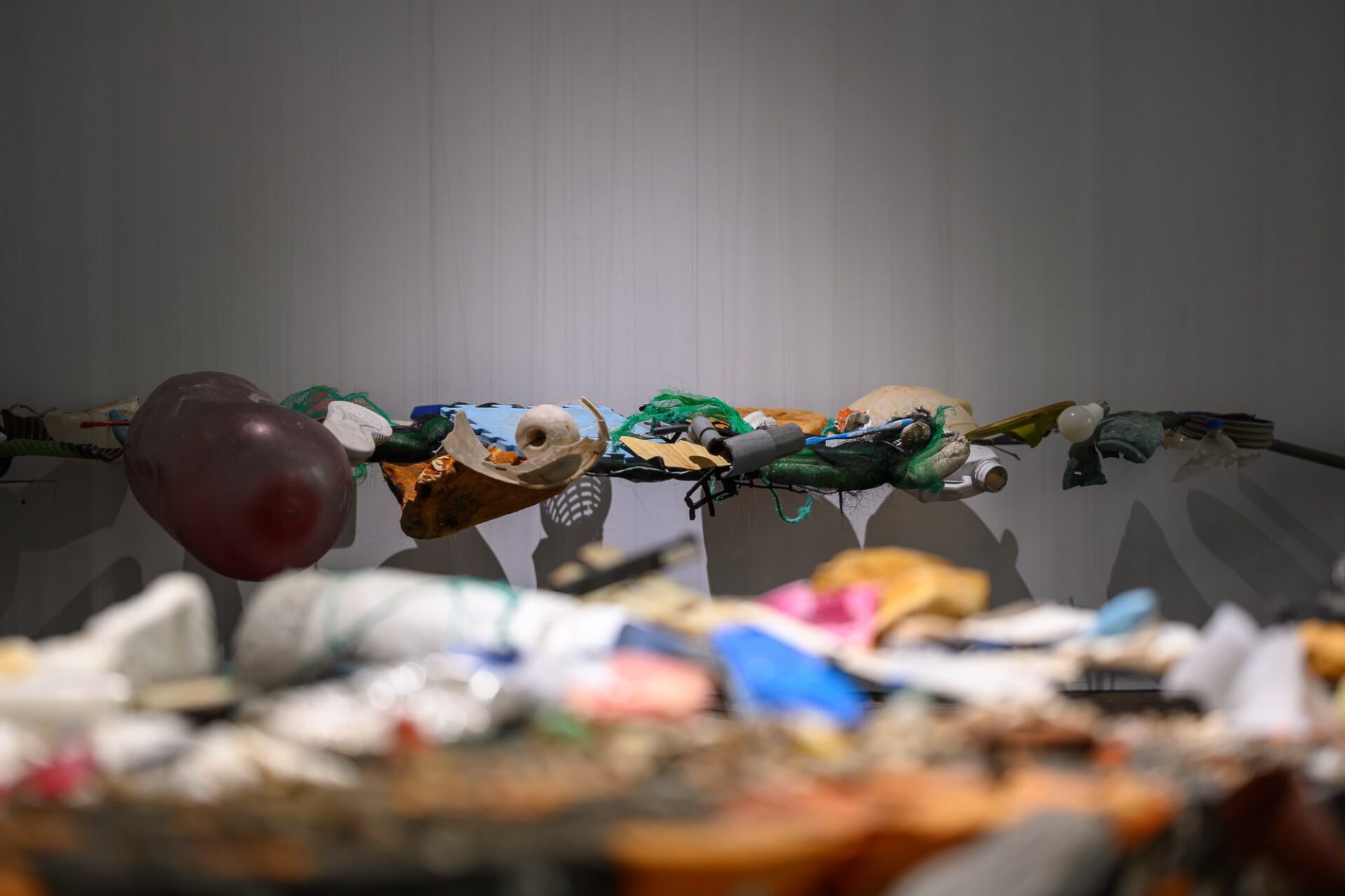 Close view through the colourful suspended objects against a pale gallery wall.