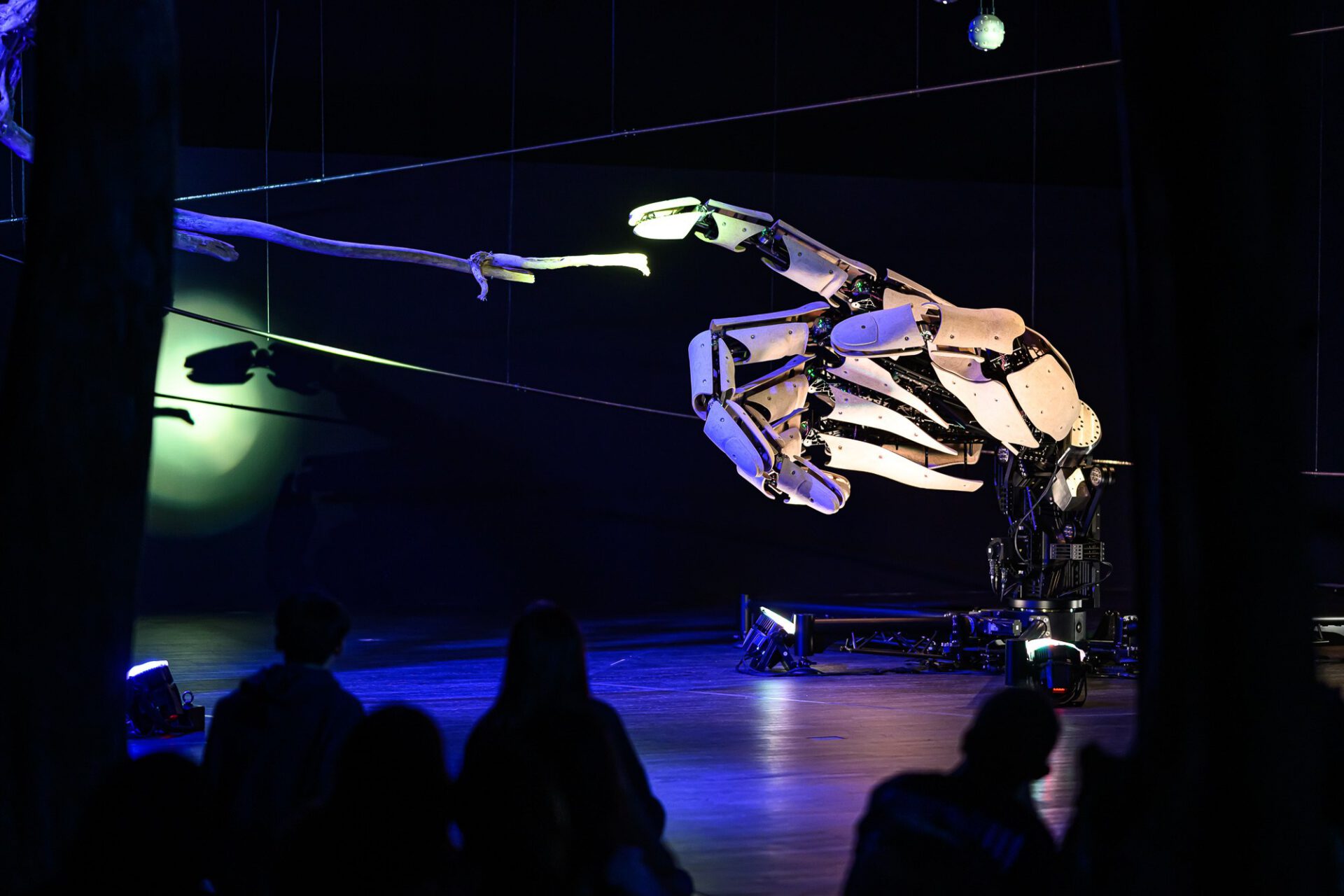 Mechanical hand extended above silhouetted visitors in the dark installation.