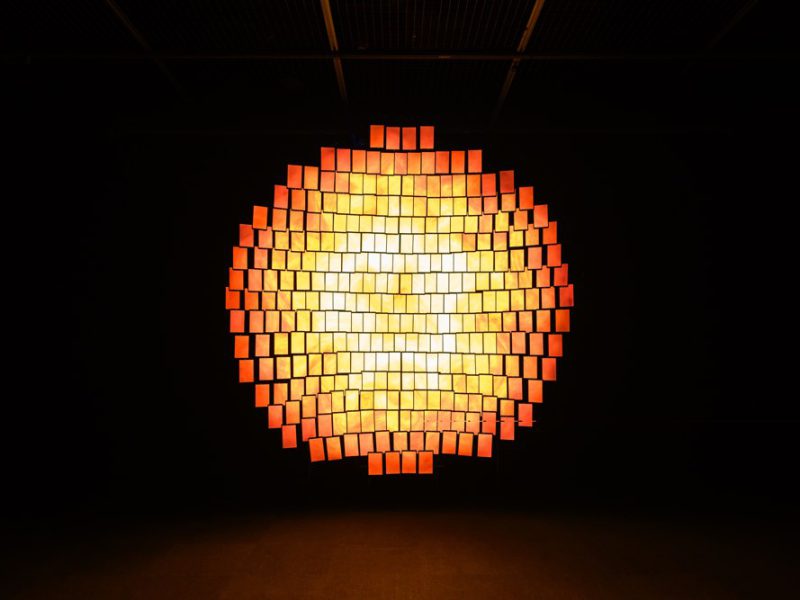 Glowing circular arrangement of illuminated rectangular screens in a dark room.