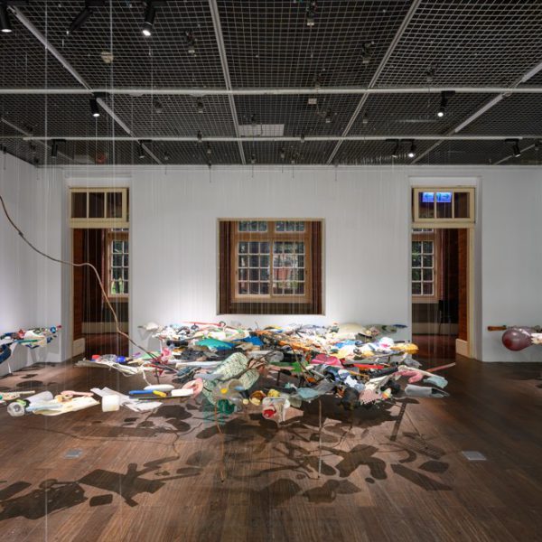 Suspended assemblage of colourful objects casting shadows across a gallery floor.